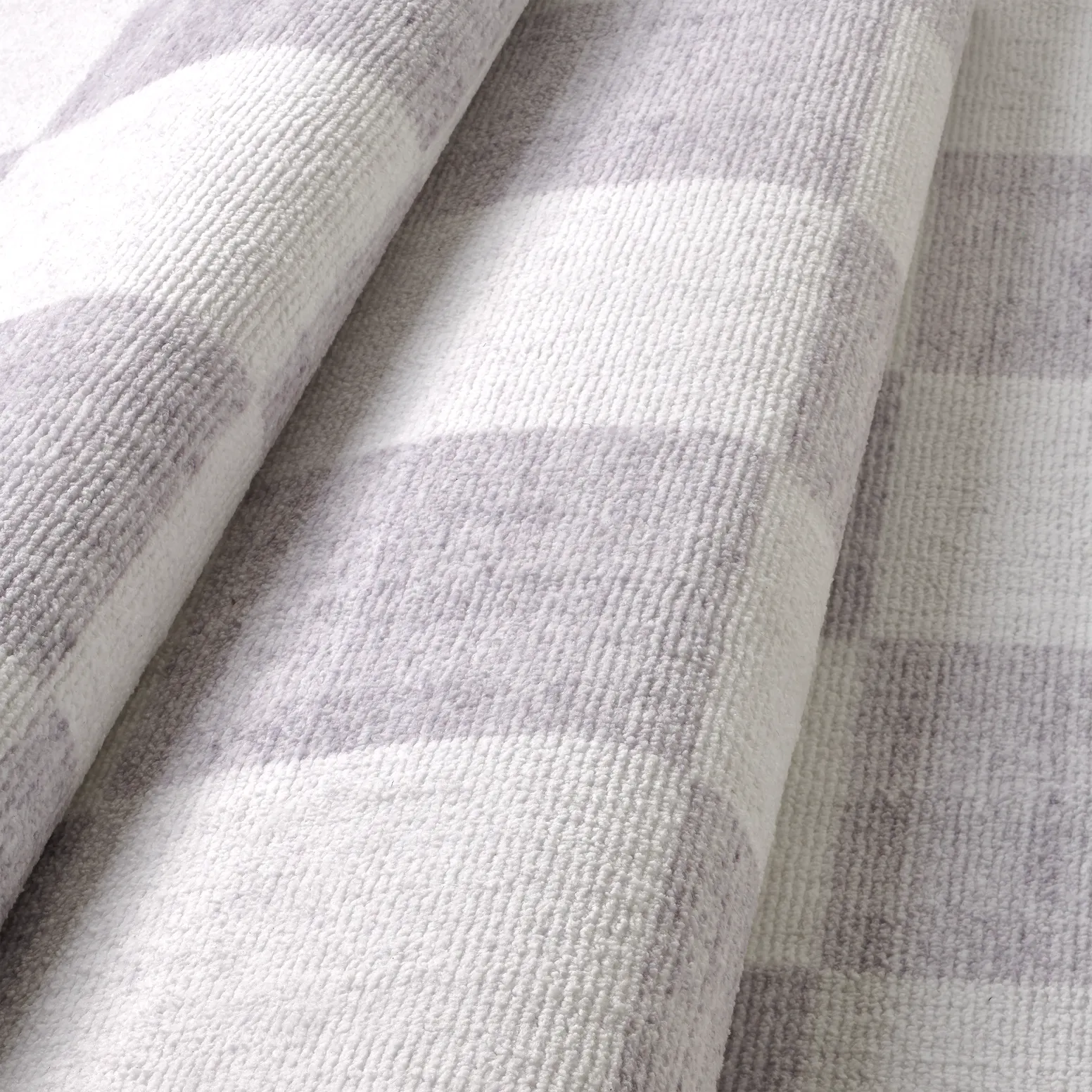 Dettaglio onda del tappeto Jack LtGrey in pelo taftato, superficie morbida effetto velluto con quadri grigio chiaro e panna.