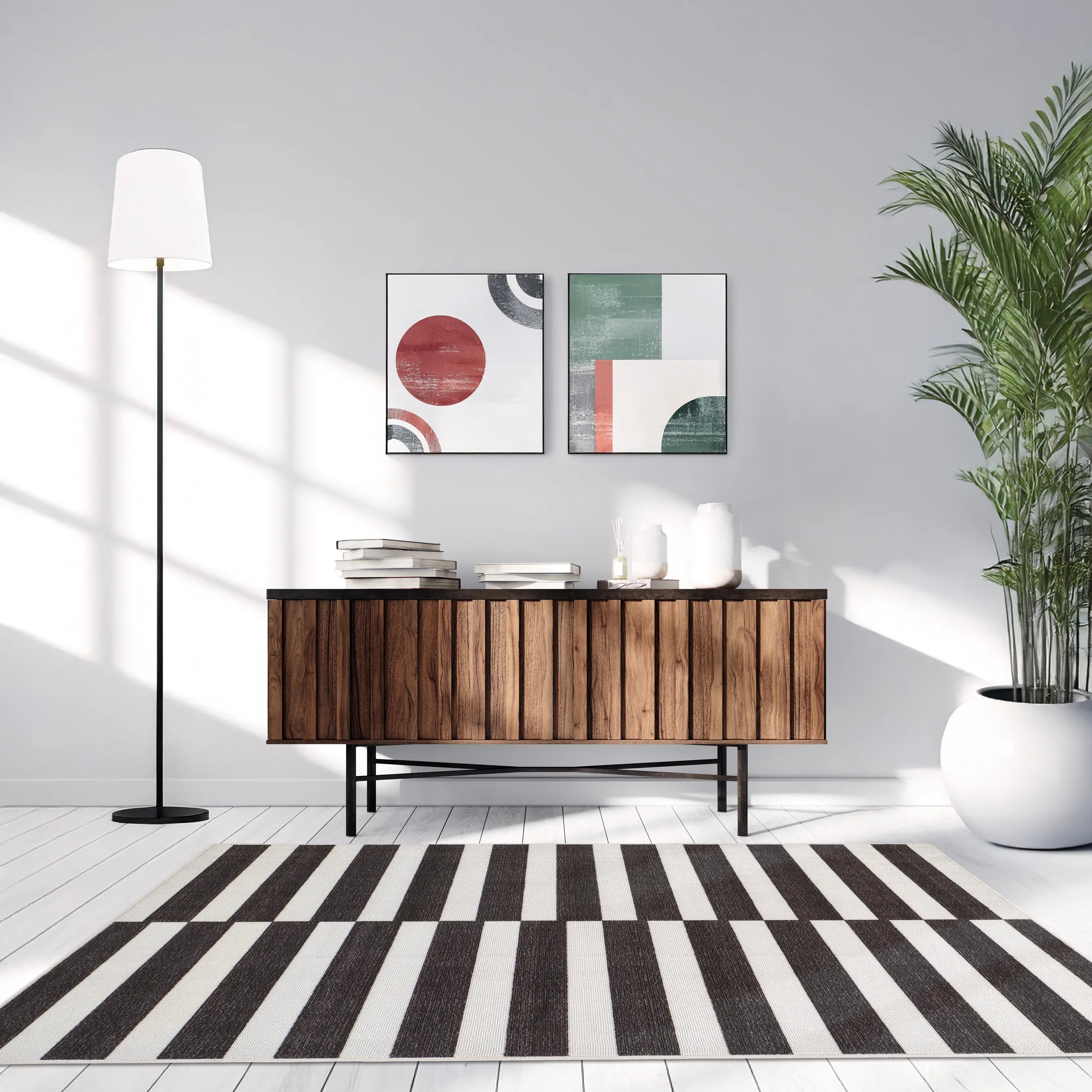 Tappeto Strider Black 130×190 cm a righe nere e panna alternate in soggiorno moderno con madia in legno, due quadri astratti colorati, pianta verde in vaso bianco e lampada da terra.