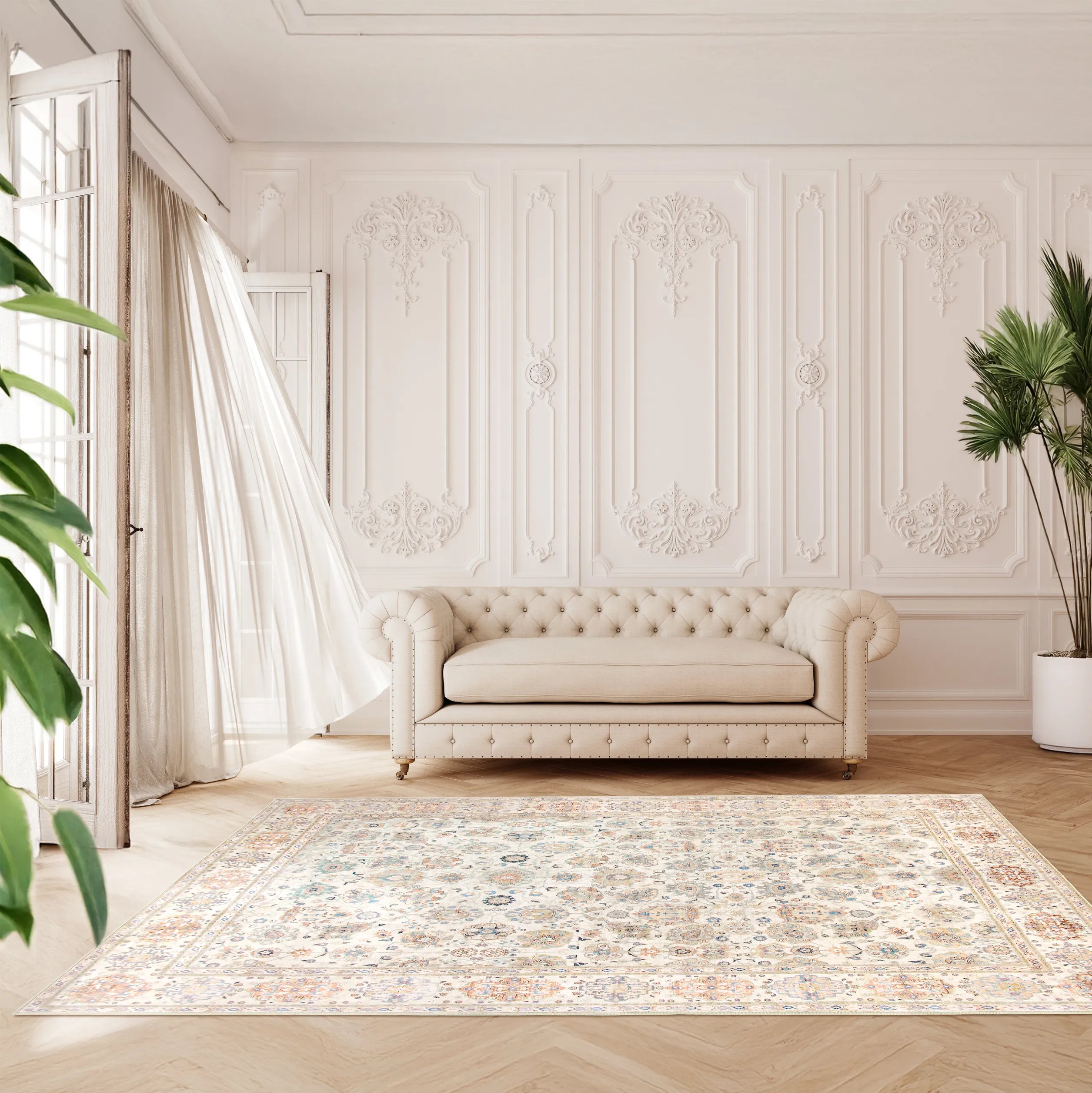 Tappeto Jane 200×290 cm in soggiorno elegante con divano capitonné beige, boiserie chiara decorata, tenda leggera mosso dal vento e piante verdi ai lati.