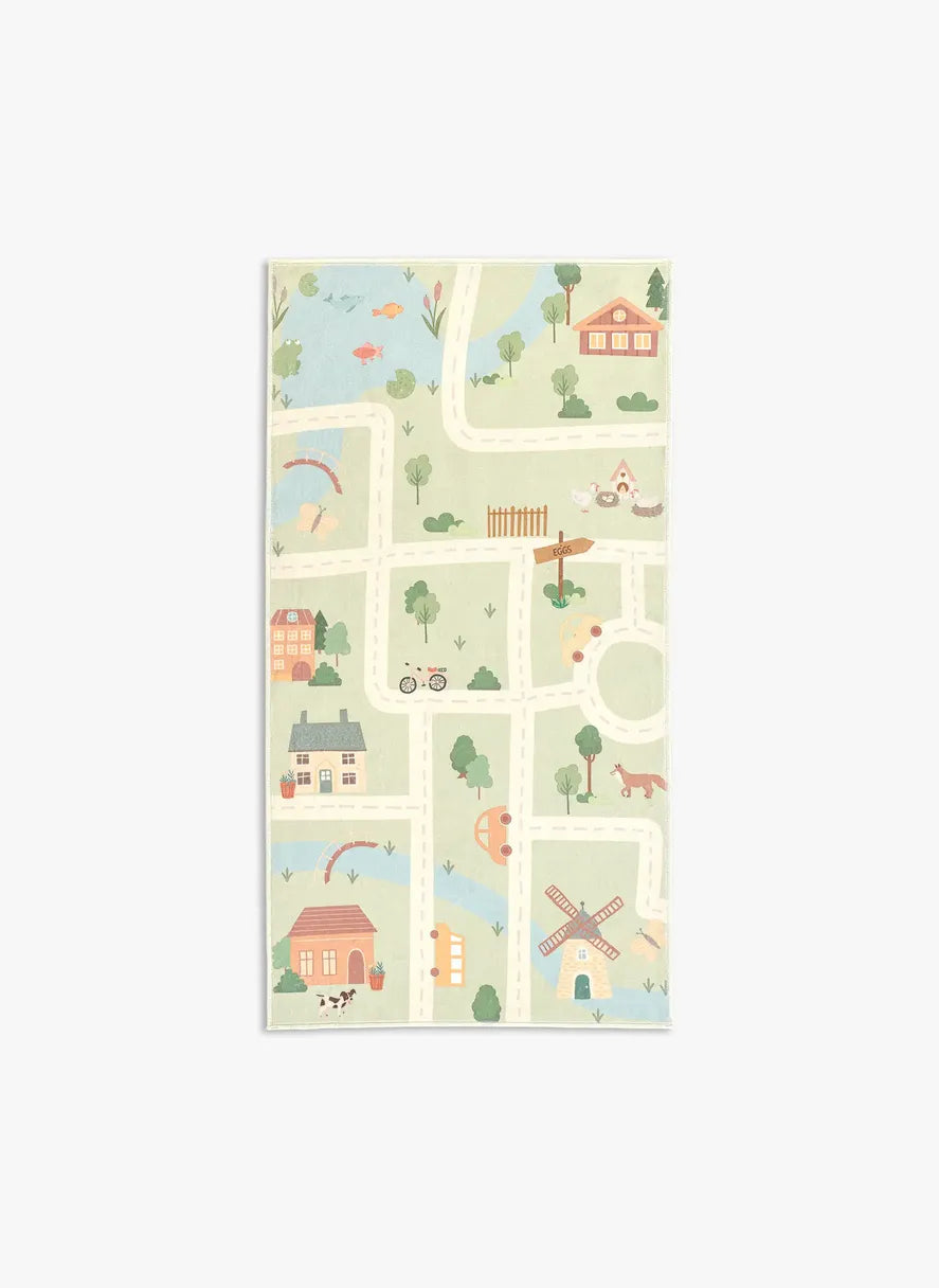 Tappeto Ecovia 80×150 cm in pelo corto di microfibra con porzione di mappa illustrata, strade bianche che attraversano casette e alberi su prato verde, visto dall’alto.