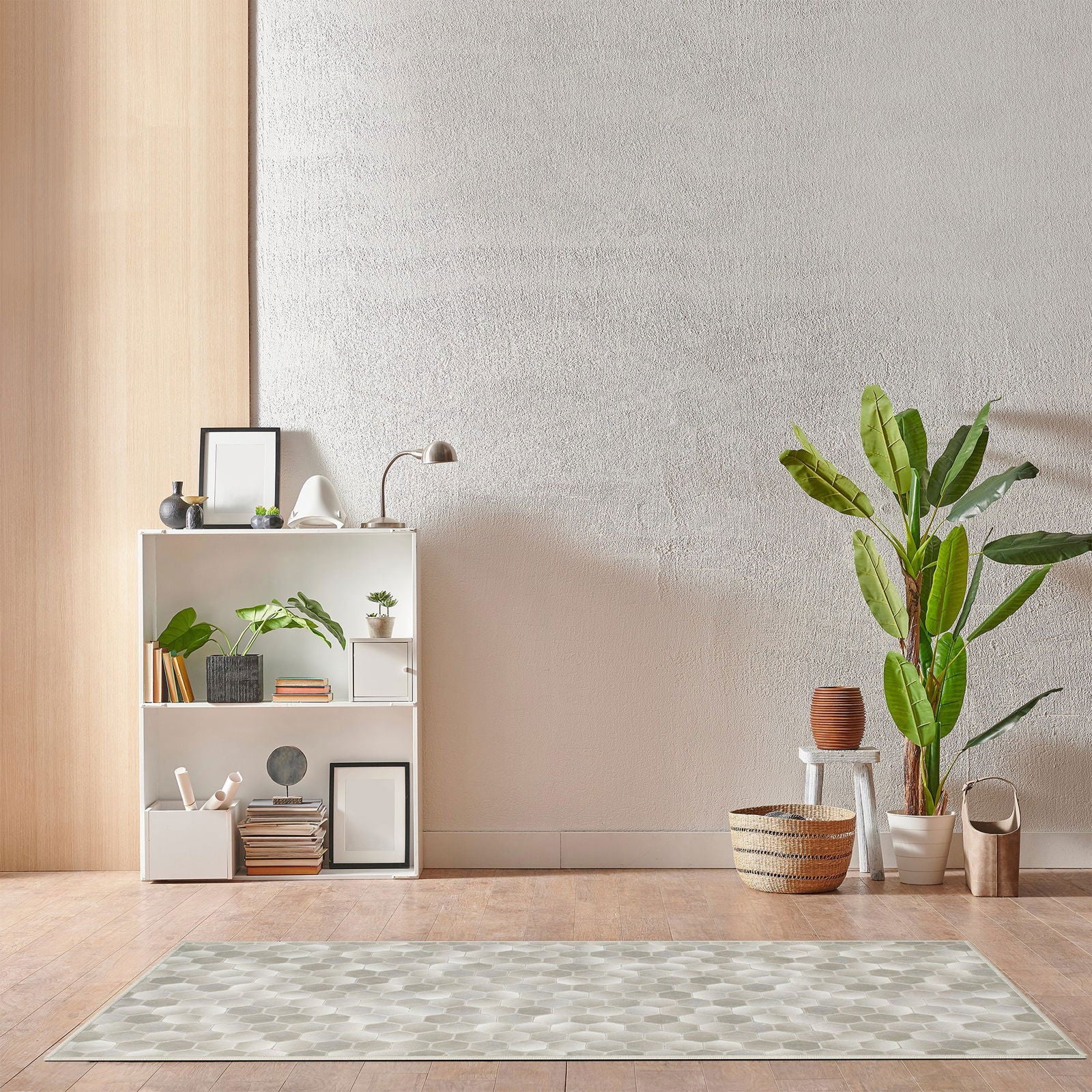 Tappeto Cotto 90×160 cm disteso su pavimento in parquet chiaro davanti a una libreria bianca e piante, con motivo esagonale sfumato tra toni di beige e grigio