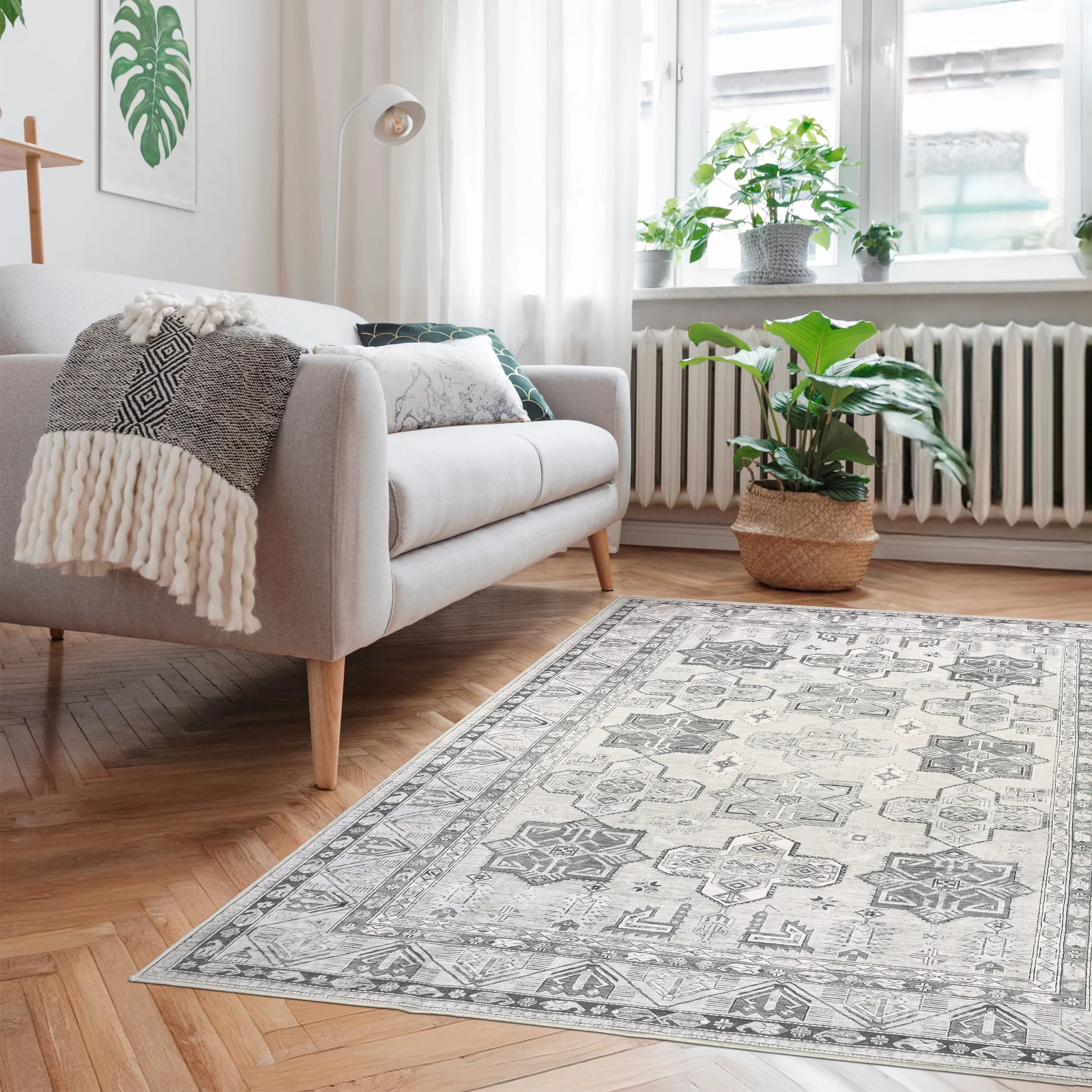 Tappeto Diamond 130×190 cm avorio e grigio con motivo geometrico caucasico, posto davanti a un divano grigio in un soggiorno luminoso con pavimento a spina di pesce.