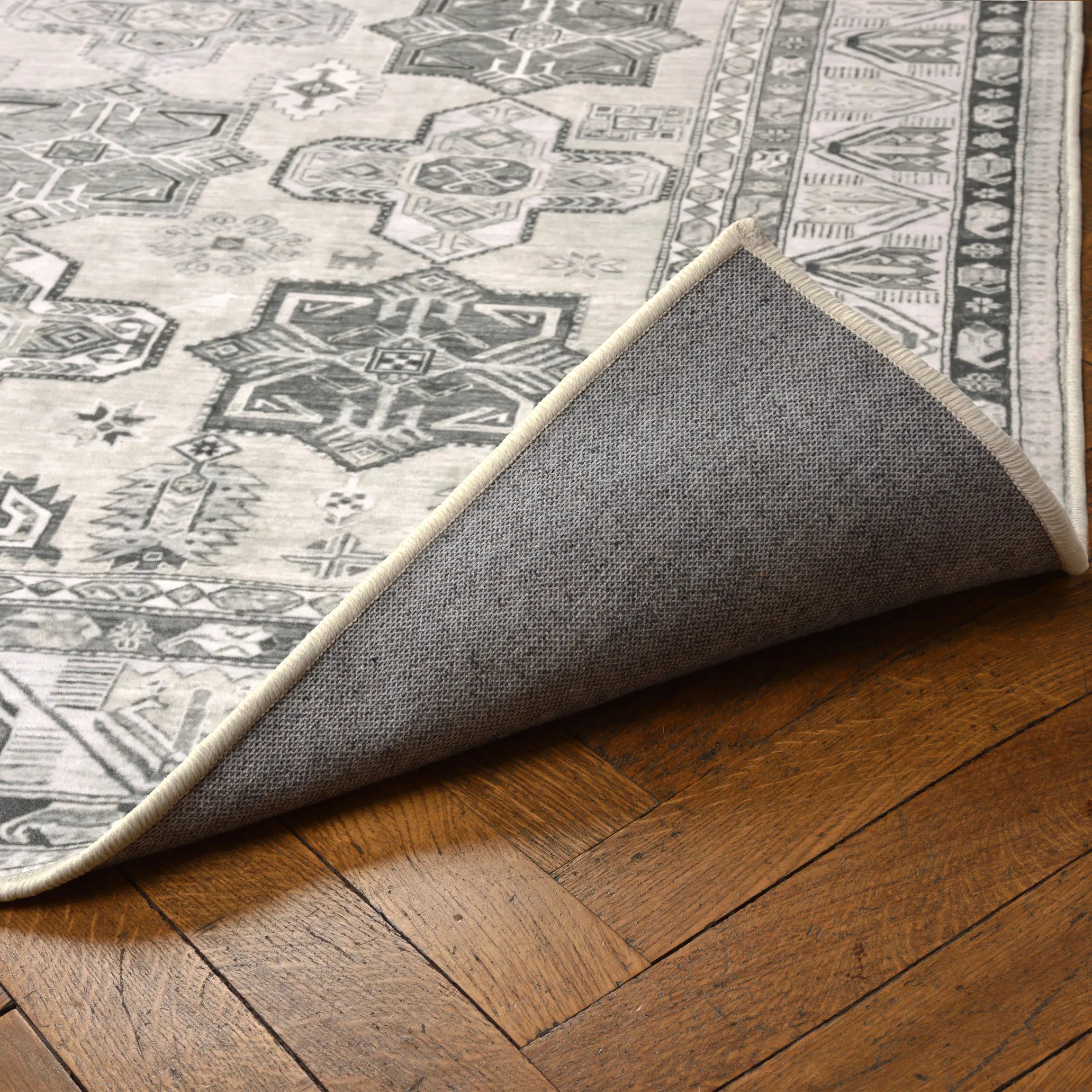 Angolo del tappeto Diamond sollevato per mostrare la base antiscivolo e impermeabile; pattern geometrico avorio e grigio.