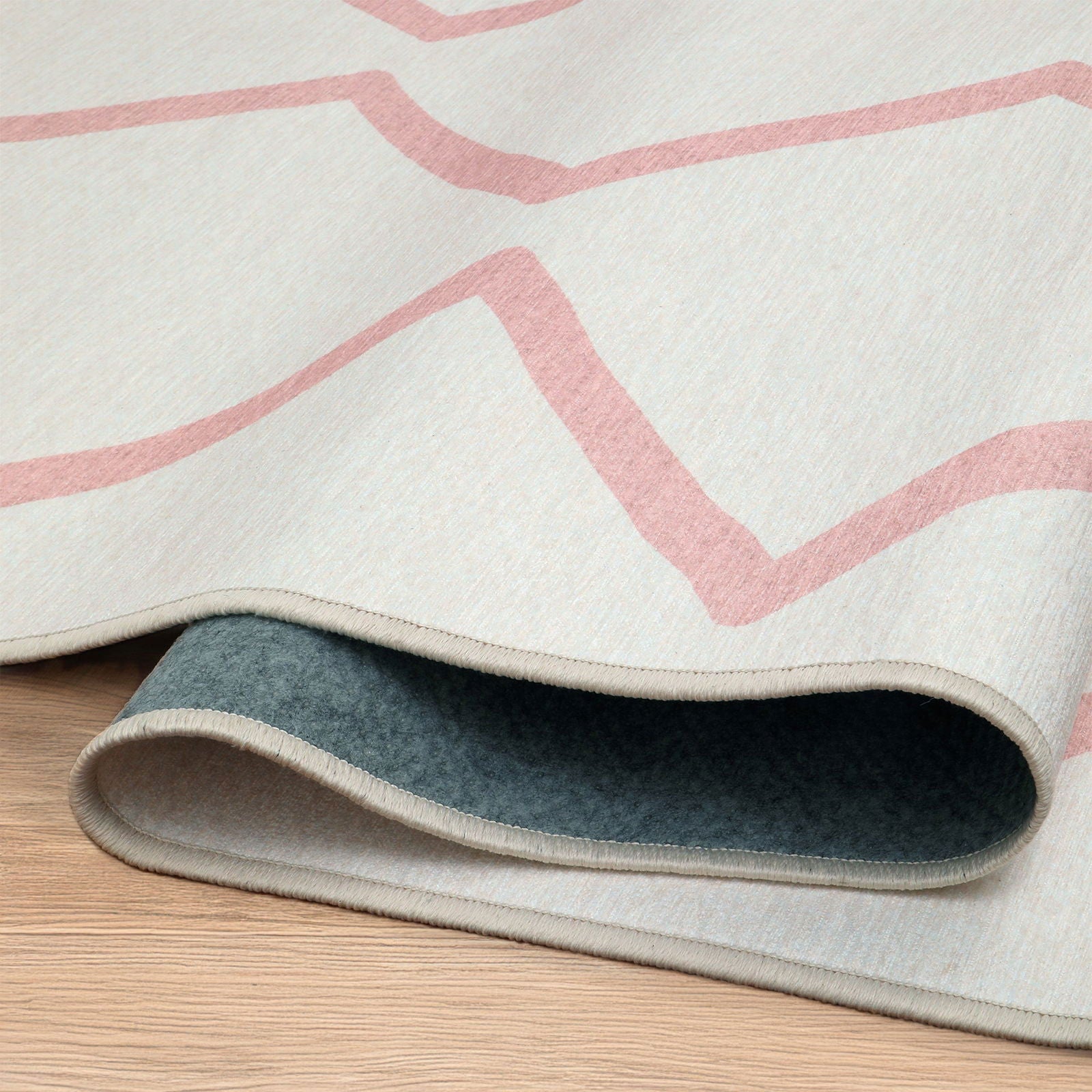 Dettaglio del retro in feltro verde-grigio del tappeto Ebro, mostrato in una piega morbida sul pavimento in legno.