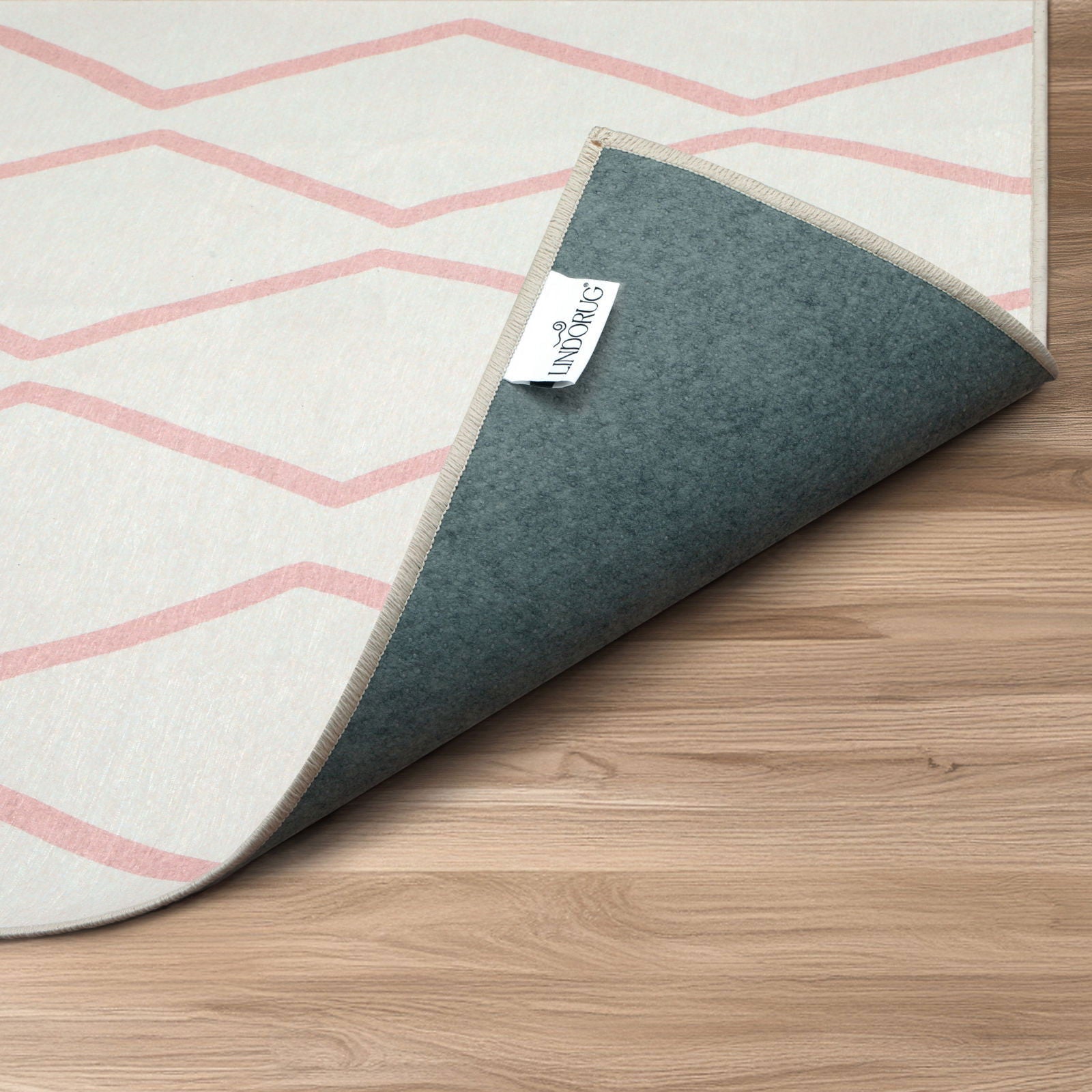 Primo piano dell’angolo arrotolato del tappeto Ebro stile Tuareg, retro grigio con etichetta bianca “Lindorug” cucita sul bordo.