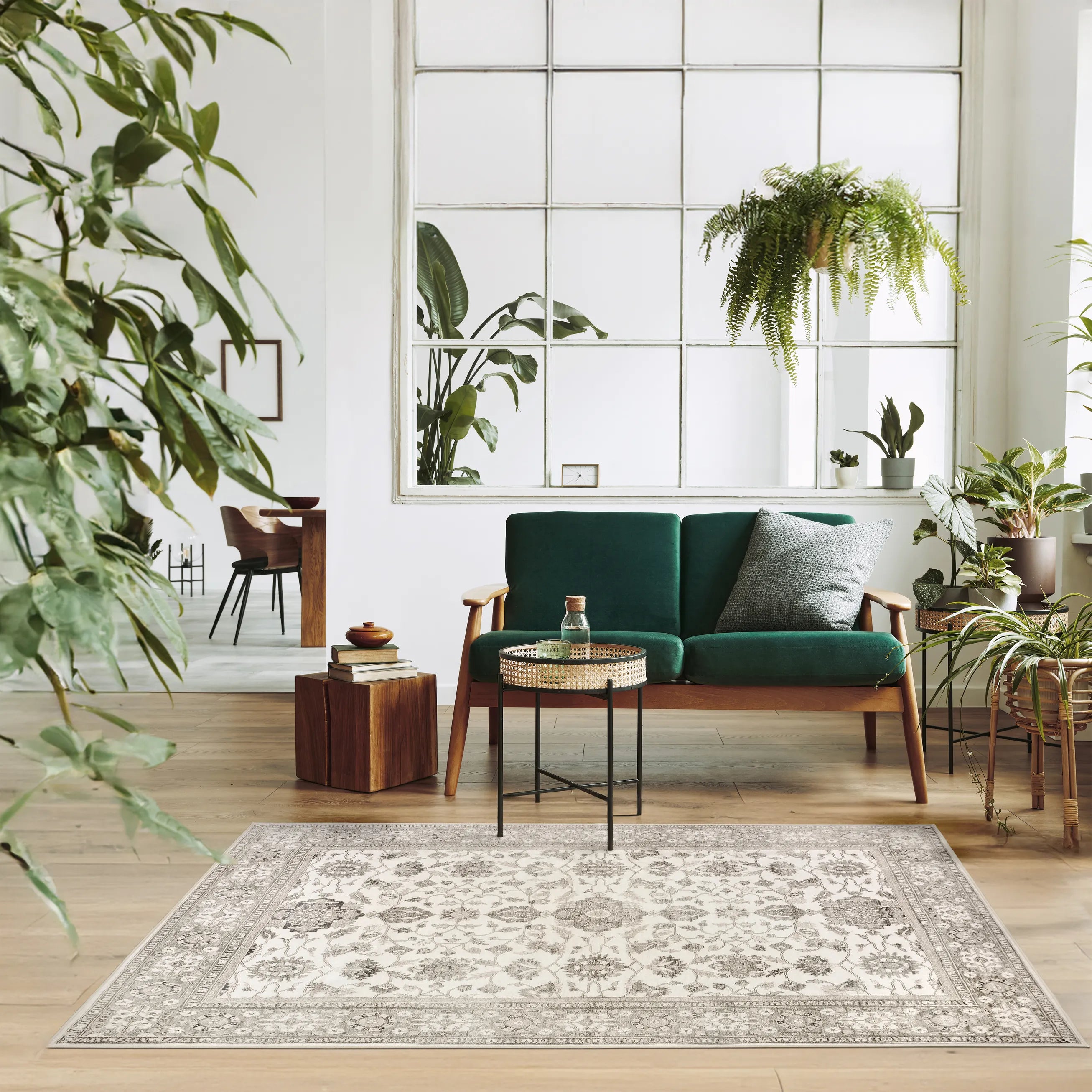 Tappeto Farah 130×190 cm con disegno floreale beige e avorio davanti a un divano verde smeraldo e numerose piante in un soggiorno luminoso; lavabile in lavatrice e asciugabile in asciugatrice.