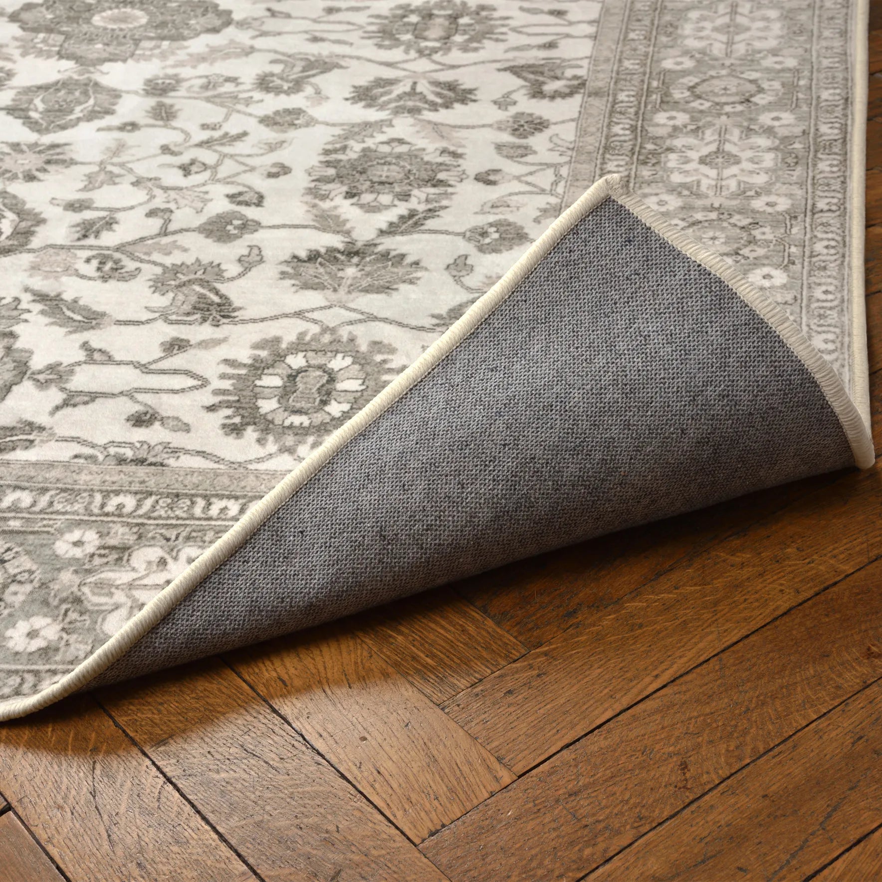 Angolo del tappeto Farah sollevato per mostrare la base antiscivolo e impermeabile; design floreale su base avorio e beige.
