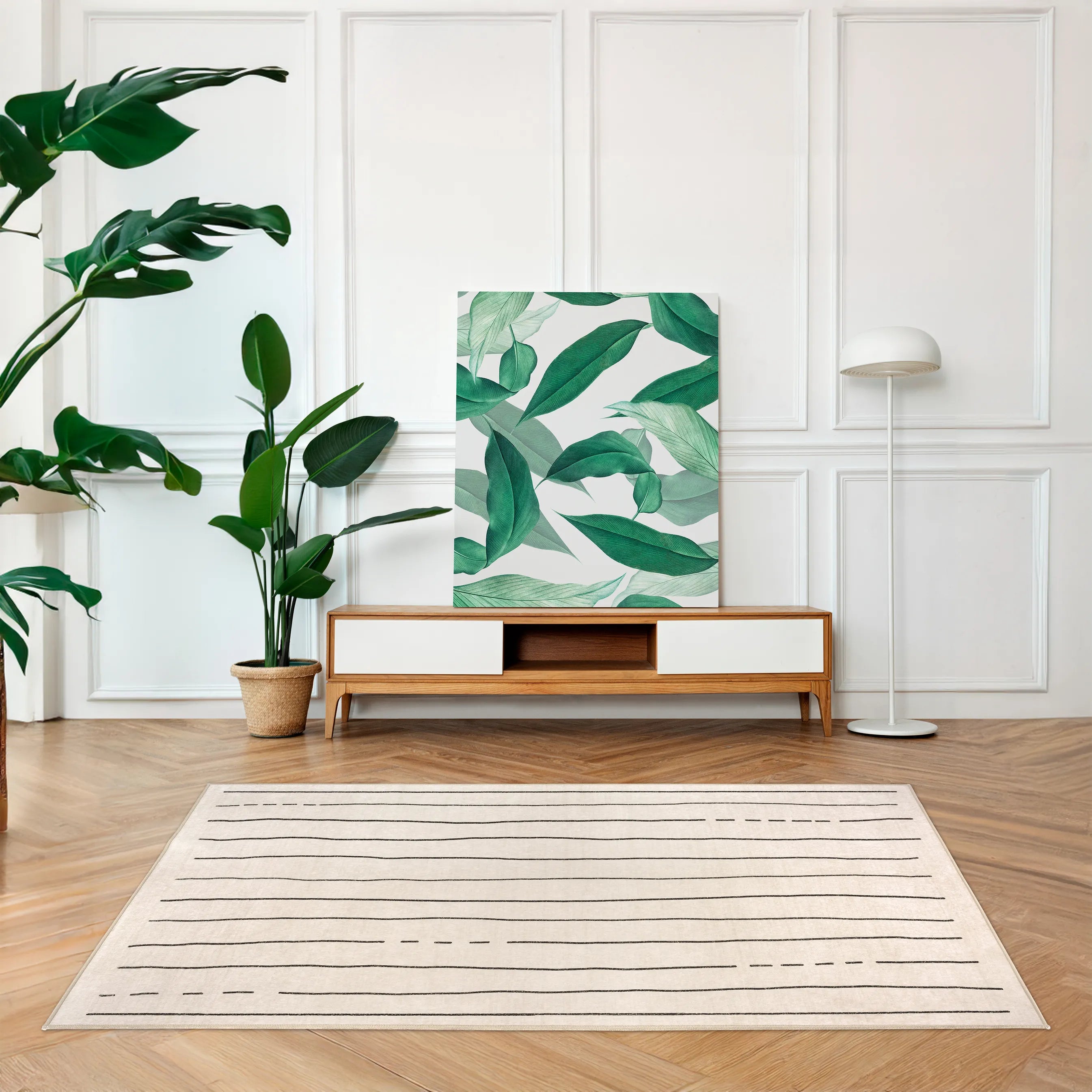 Tappeto Lead 130×190 cm con righe nere su fondo crema, ambientato con mobile basso in legno e tela botanica; lavabile e asciugabile.