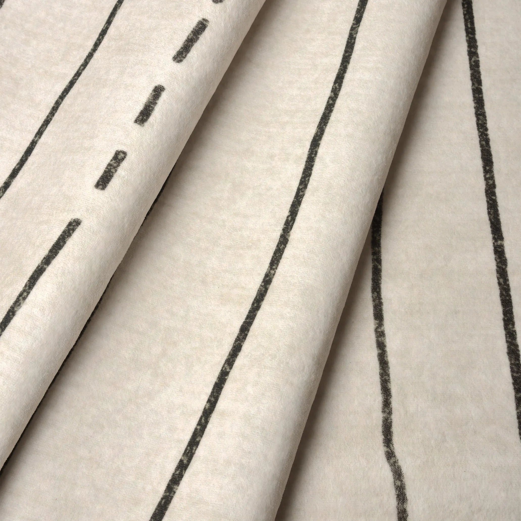 Dettaglio del tappeto Lead: superficie vellutata color crema con righe nere, motivo tuareg.