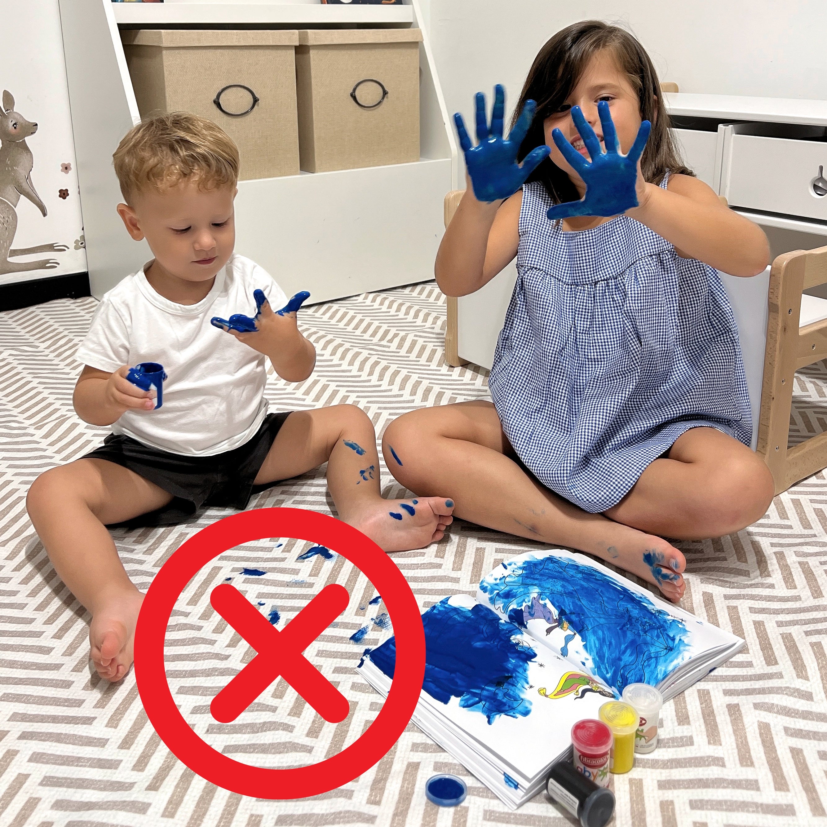 Due bambini che sporcano con pittura blu un tappeto Lindorug a motivo geometrico, con una X rossa sovrapposta per indicare il divieto