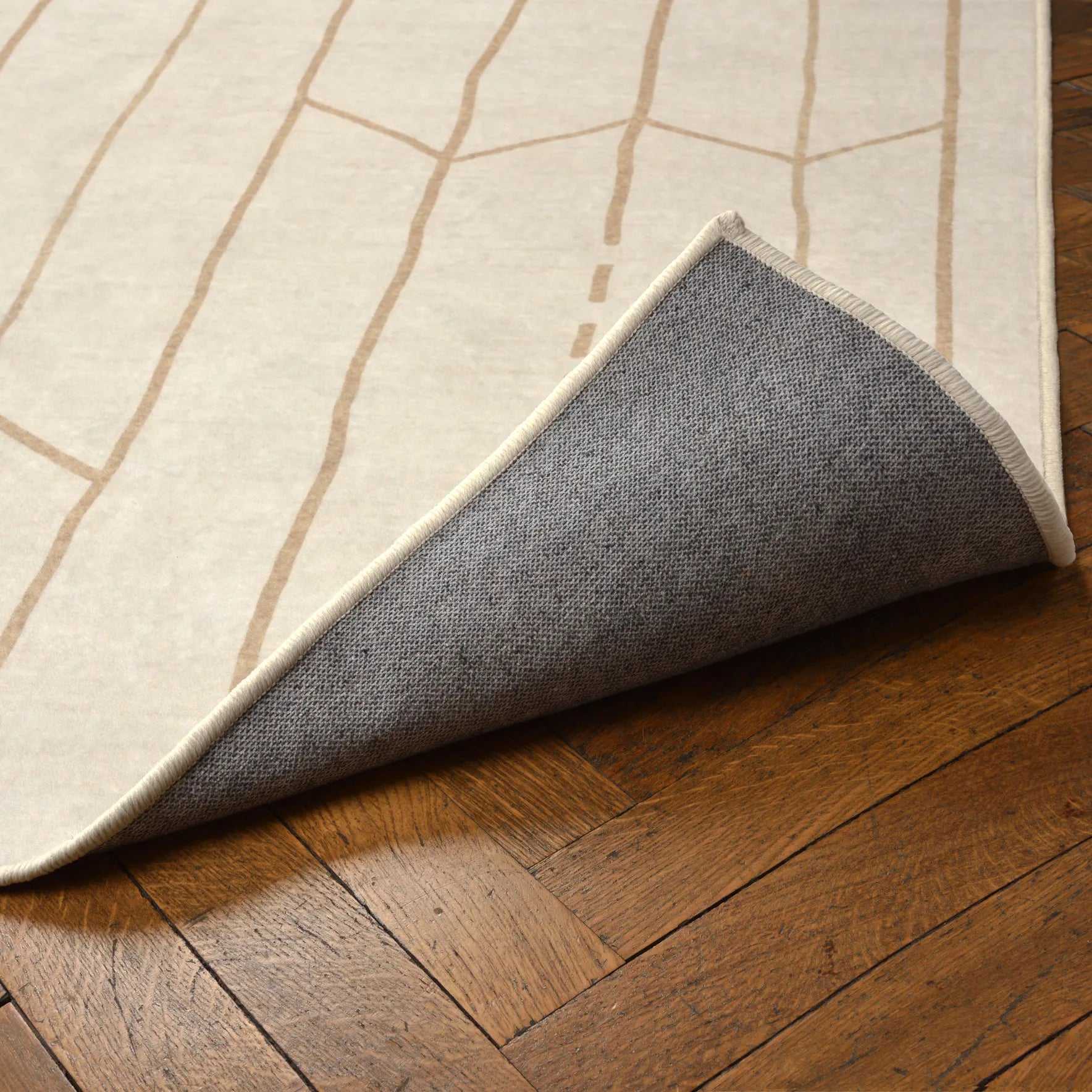 Angolo sollevato del tappeto Maira che mostra la base antiscivolo e impermeabile; pattern tribale beige su superficie crema lavabile e asciugabile.