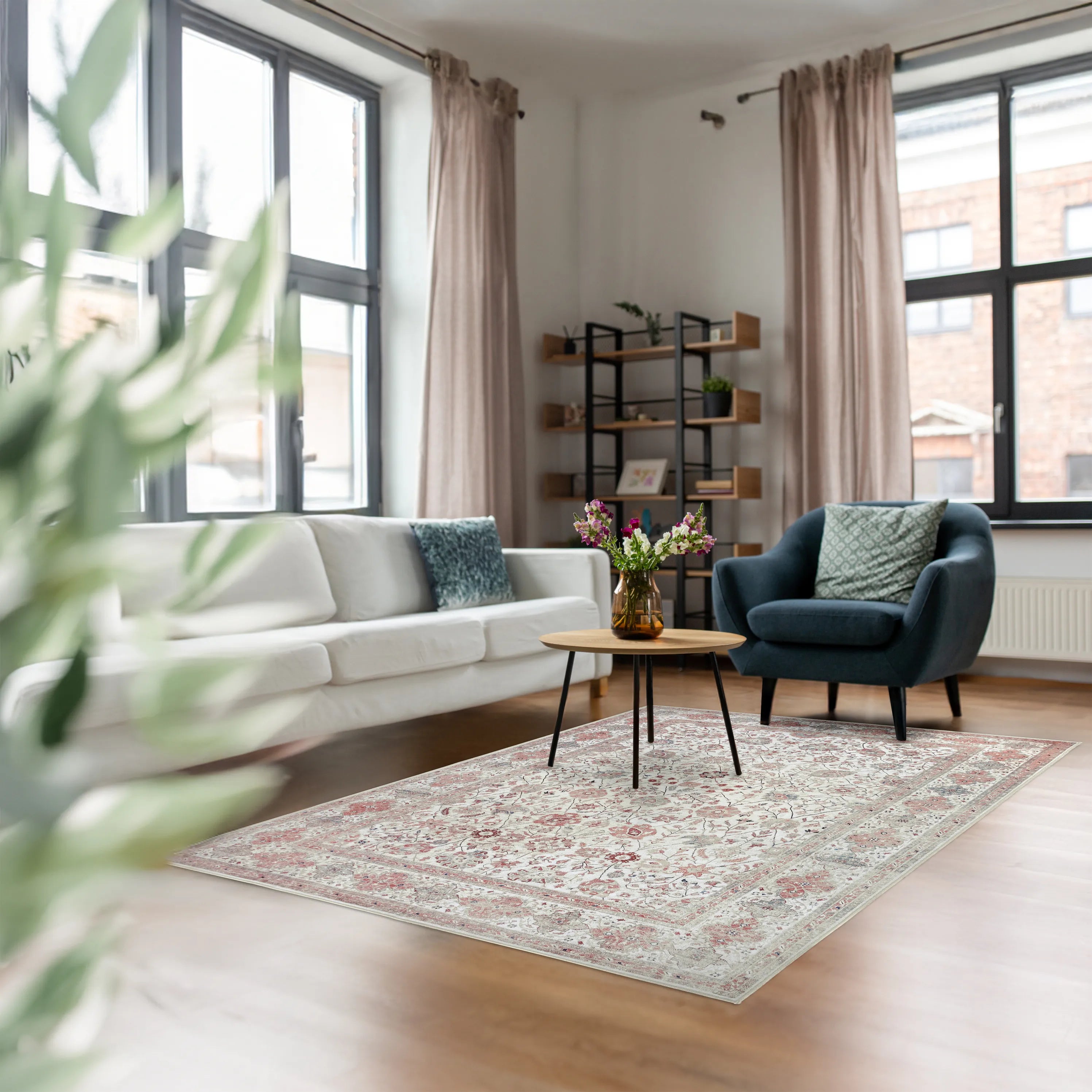 Tappeto Sindhi 160 × 230 cm ecru e corallo posizionato in un salotto moderno con divano bianco e poltrona blu; motivo floreale e stile orientale.