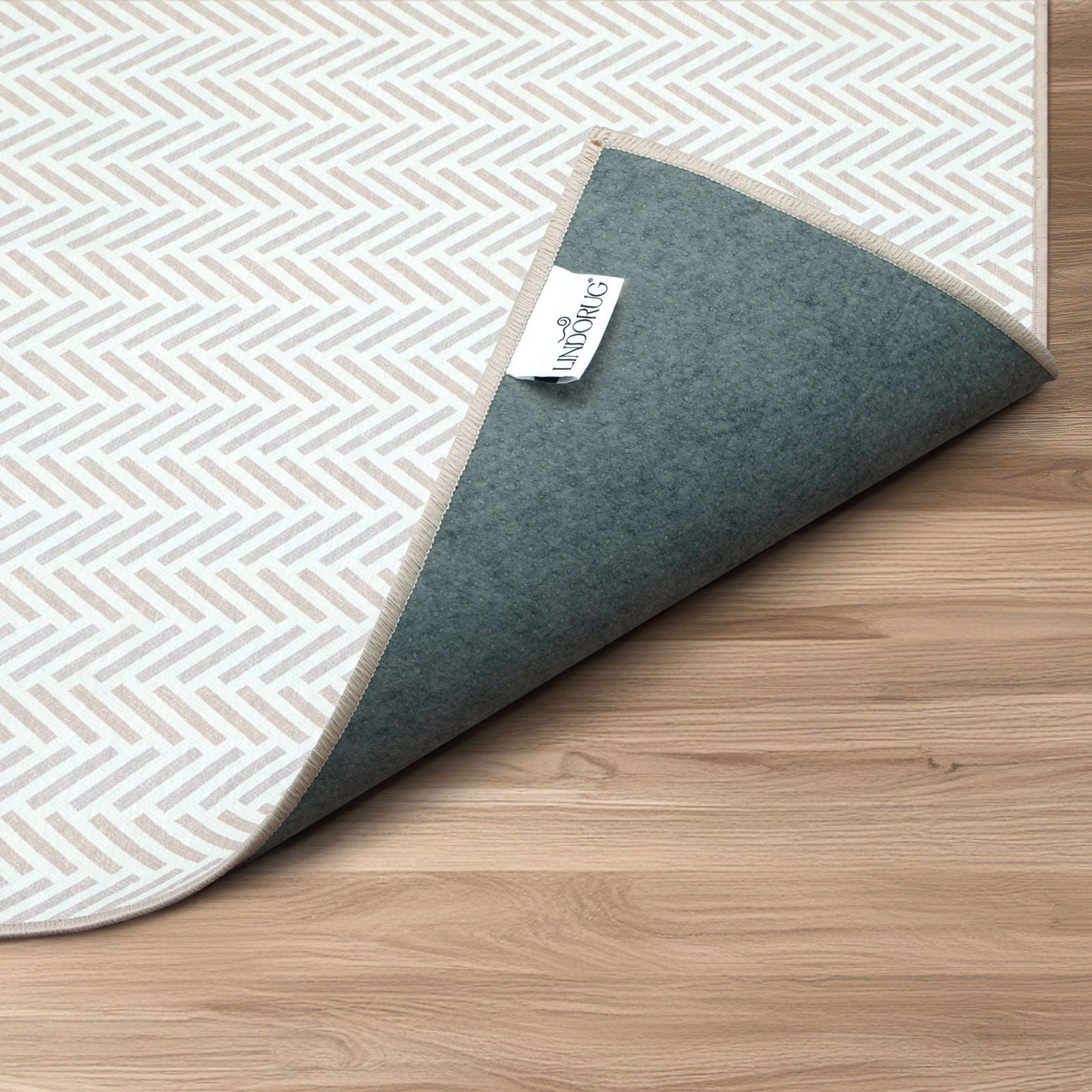 Dettaglio angolo piegato del tappeto Lindorug Spiga collezione Chenny con motivo a spina di pesce, retro antiscivolo e etichetta Lindorug